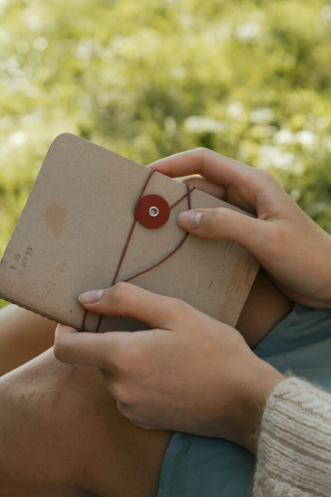 A woman holds a vintage notebook on her lap while sitting outdoors in summer.